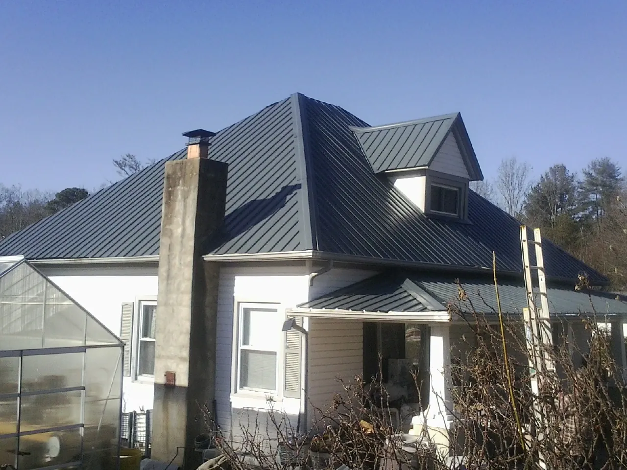 Dark blue standing seam metal roof on a white farmhouse with dormer — Slate & Tile Roof Repair by Roofing Brothers in Loretto