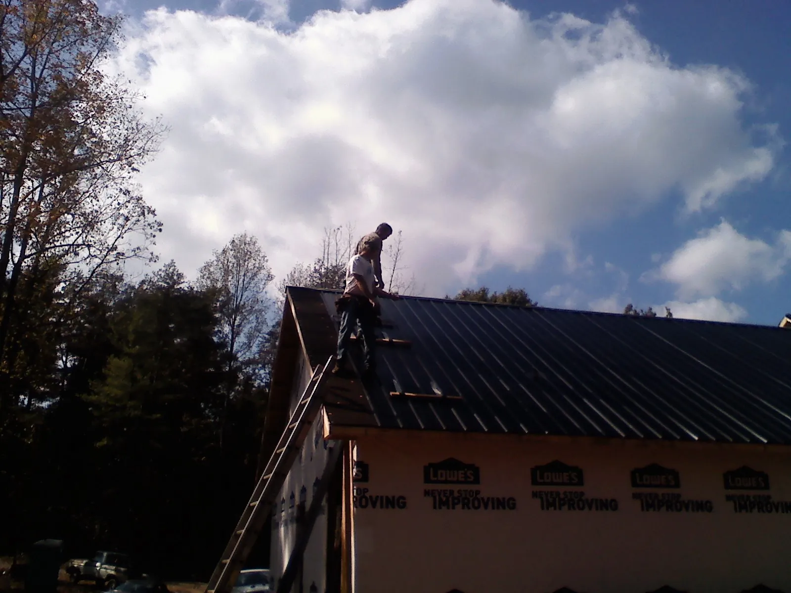 Roofer fastening dark metal panels high against a cloudy sky, from a Roof Inspection job in Loretto